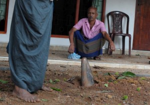 Residents look on as a mortar shell is seen lodged in the compound of a home at Salawa on the edge of the Sri Lankan capital Colombo on June 6, 2016, hours after an explosion of an ammunition depot at the neighbouring military complex. Flying shrapnel triggered by explosions at an ammunition depot on the edge of Sri Lanka's capital Colombo sent thousands of residents scrambling for cover as the blaze turned the skies orange Monday. The explosions went on for over 12 hours following the worst fire at a Sri Lankan military armoury. / AFP PHOTO / ISHARA S.KODIKARA